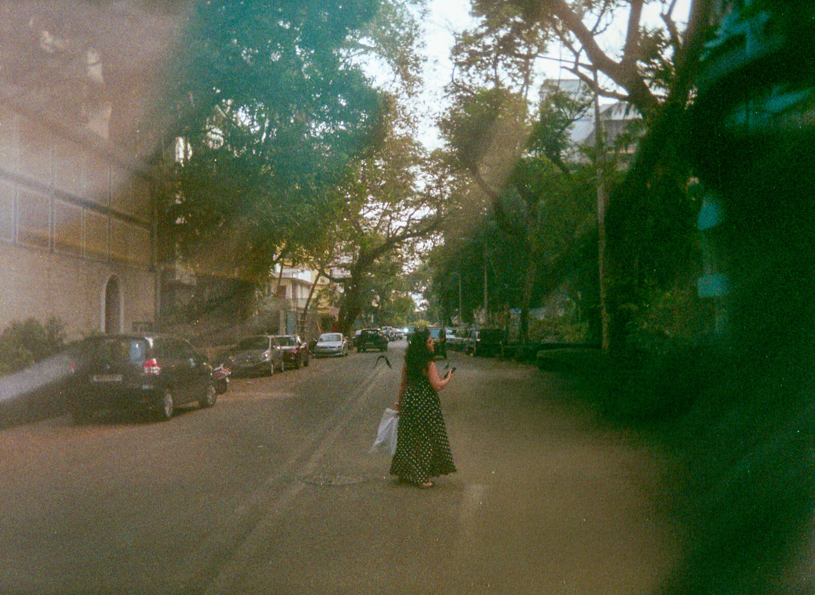Woman in a polka-dot dress on a tree-lined street with lens flare