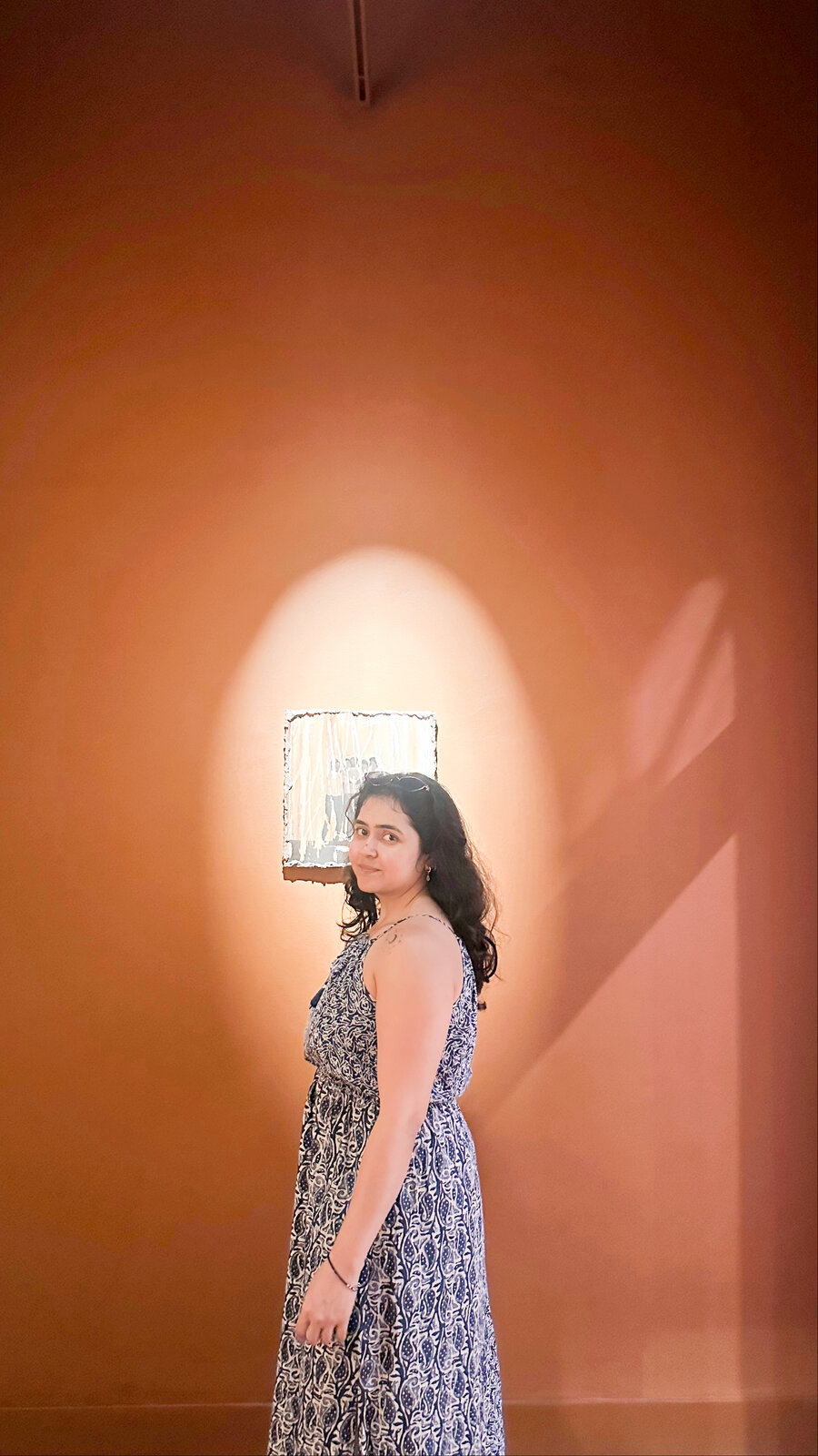 A figure in a patterned dress under warm gallery light