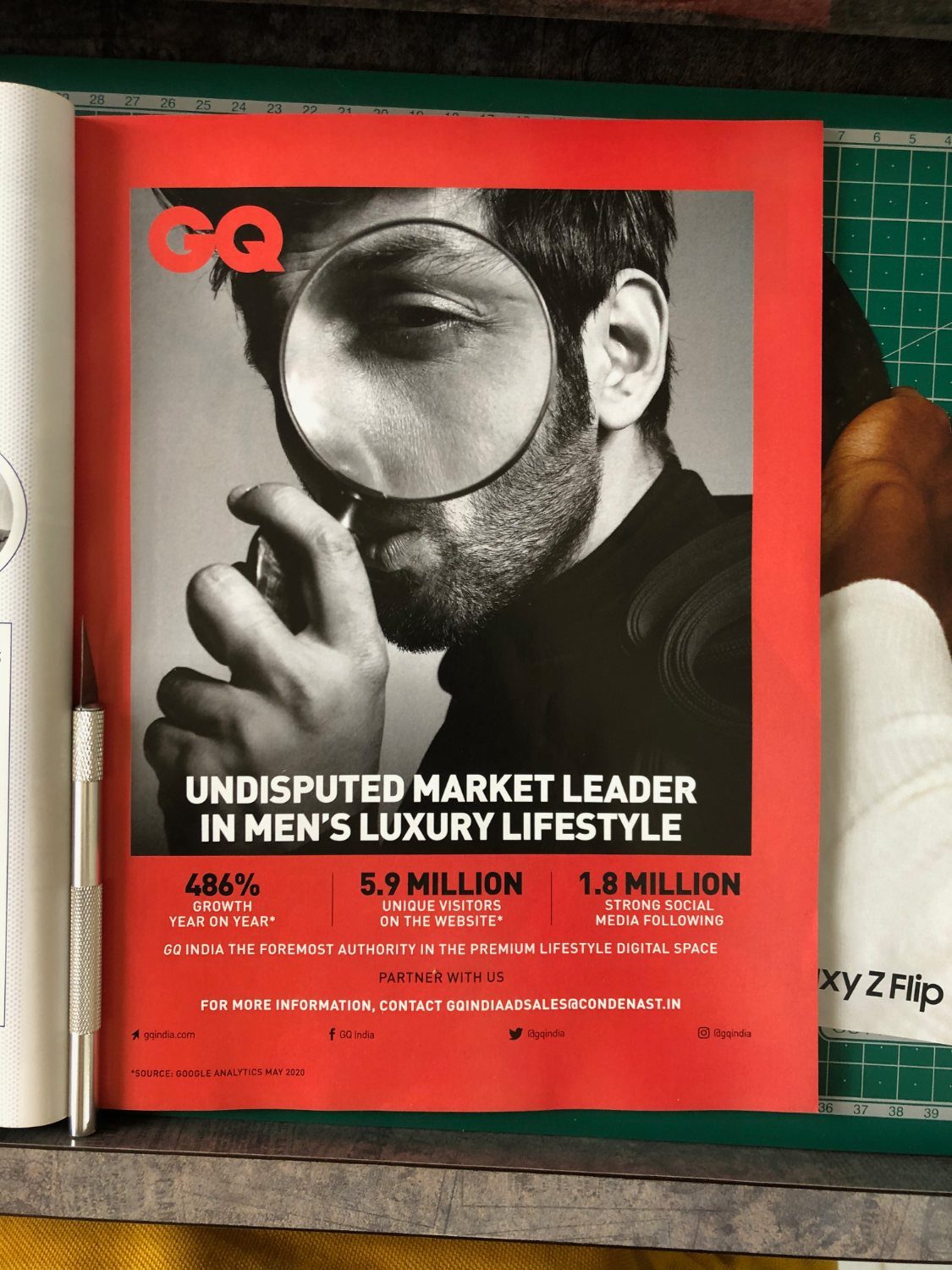 GQ India full-page house advertisement: a man examining the camera through a large magnifying glass, on a red background